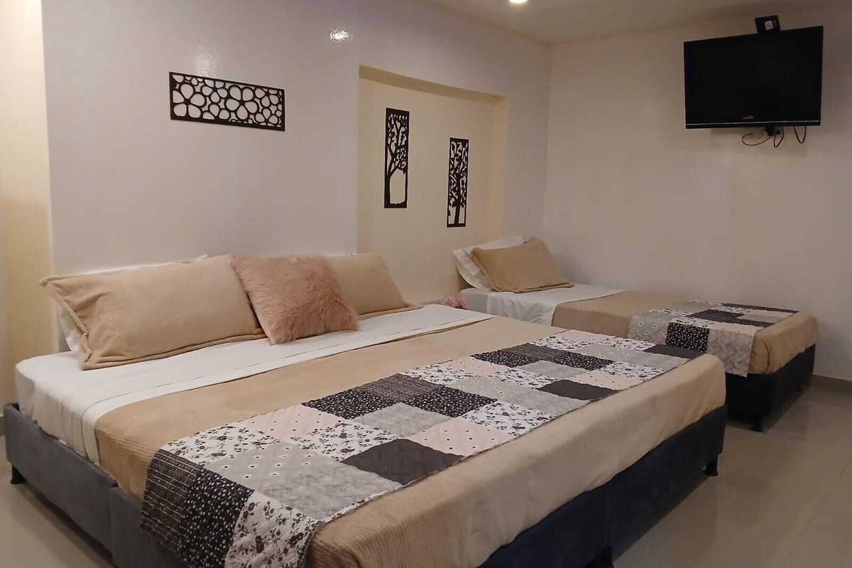 Habitación de hotel con dos camas, cada una con cubrecama acolchado y almohada mullida. Hay un televisor de pantalla plana montado en la pared y decoración artística en la pared sobre las camas.