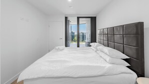A modern bedroom with a large bed, a dark headboard, and a view of buildings through a glass door.