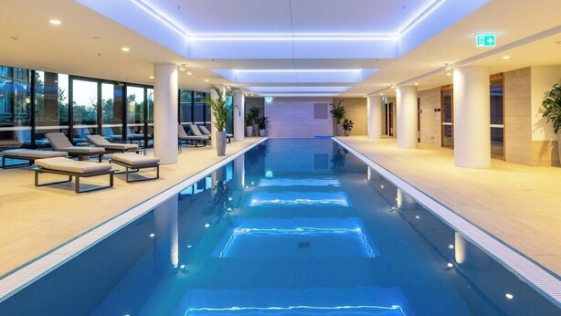 A modern indoor swimming pool with lounge chairs and a view of the city.