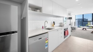 A modern kitchen with white cabinetry, a dishwasher, and a sink. There is a window with a view of buildings.