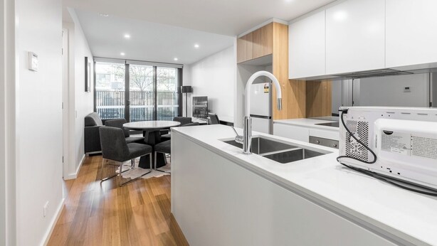 A modern kitchen with white cabinetry, a built-in microwave, and a dining area with a round table and chairs.