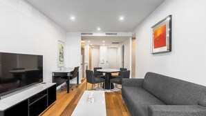 A modern living room with a flat-screen TV, grey sofa, dining table with chairs, and a coffee table.