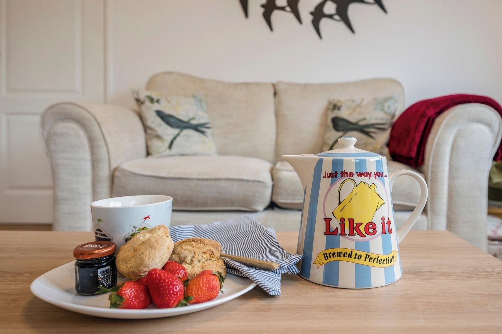 Un salón acogedor con un sofá, una mesita de centro, una taza, un hervidor, galletas y fresas.