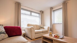 A cozy room with a sofa, a red chair, a small table with a tray of fruit, and a window with blinds. - 21 Chapel Road, Wrentham (Wrentham)