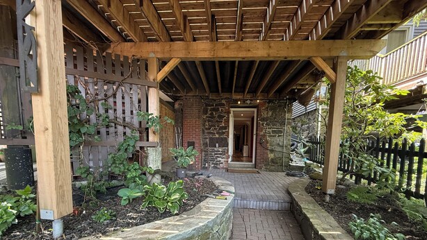 A covered outdoor area with a stone wall, wooden pergola, and a brick pathway leading to a door. - Stylish space in Victorian house located on South Park Street. Private Garden. (Halifax)