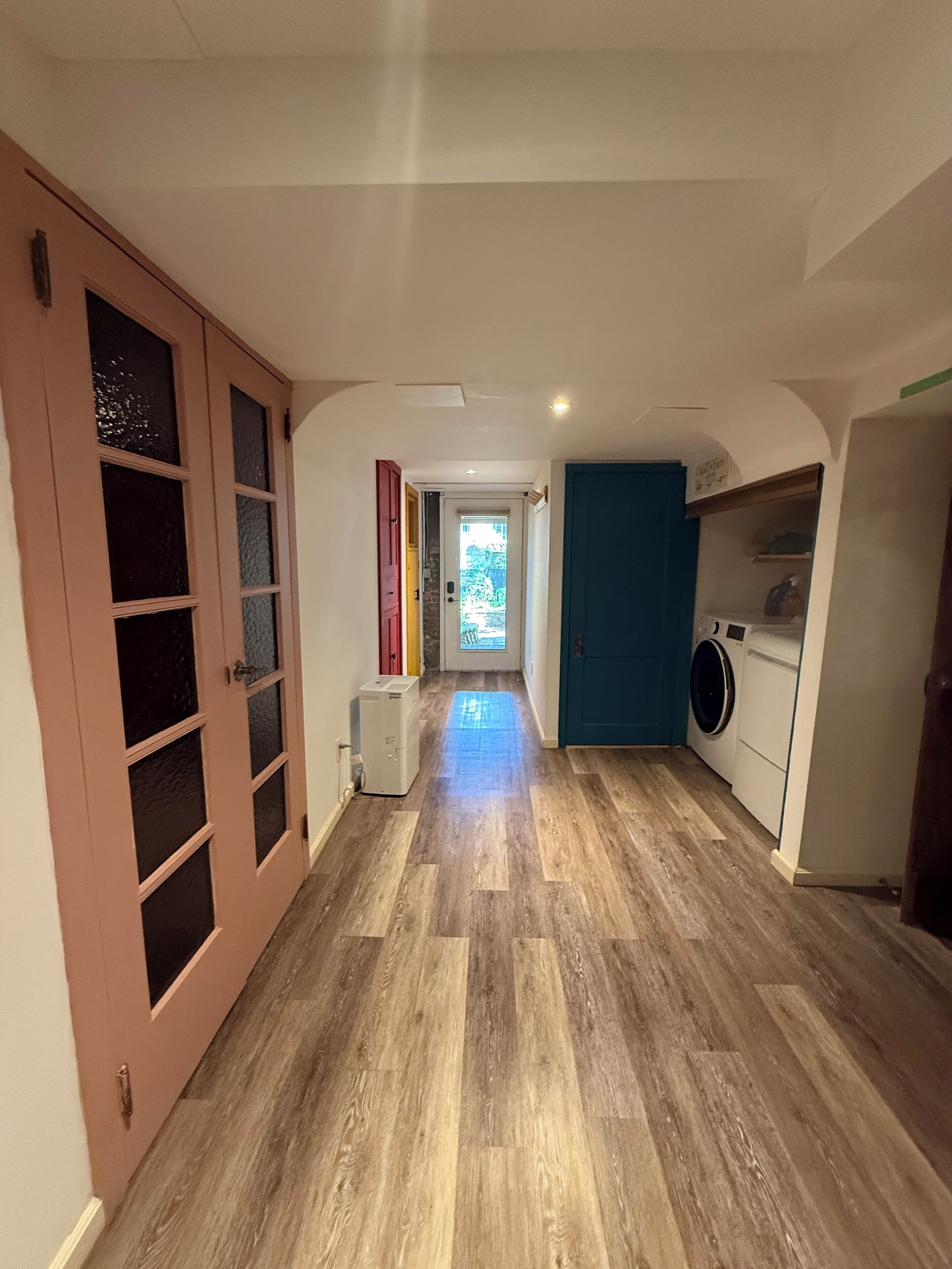 A hallway with a wooden floor, a washing machine, and a blue door.