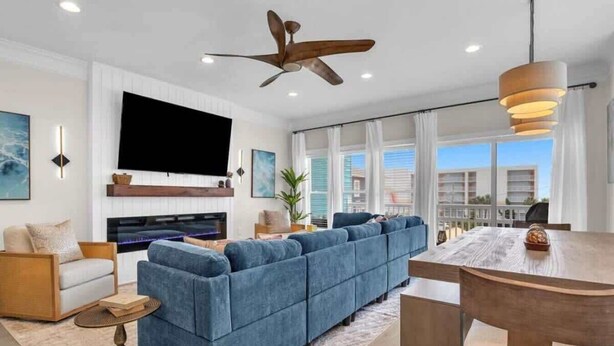 A modern living room with a sectional sofa, a flat-screen TV, a ceiling fan, and a dining area with a wooden table and chairs. - Ocean views-Steps from Beach-Elevator-3 Kings-Pets (Carolina Beach)