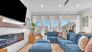 A modern living room with a sectional sofa, ottoman, and a flat-screen TV. - Ocean views-Steps from Beach-Elevator-3 Kings-Pets (Carolina Beach)