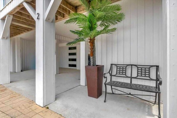 A bench and a potted palm tree in a covered outdoor area with white walls and a wooden ceiling.