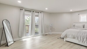 Une chambre à coucher avec un lit, un ventilateur sur pied et une grande fenêtre avec des rideaux.