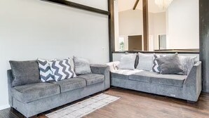 Un salon moderne avec deux canapés gris, des coussins à motifs, un plancher en bois et un grand miroir qui reflète la pièce.