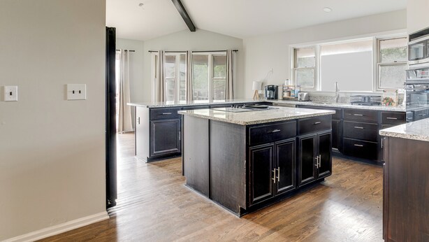 Une cuisine moderne avec des meubles de couleur sombre, un grand îlot central et une vue sur l’extérieur.