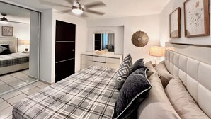 Un dormitorio moderno con cama, sofá, armario, ventilador de techo y espejo.