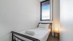 Una habitación pequeña con cama individual, ventana, lámpara de noche y radiador.