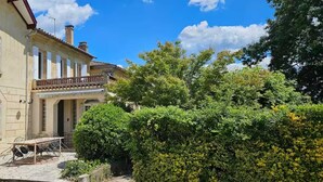 Un bâtiment à deux étages doté d’un balcon, d’une cour pavée et d’une végétation luxuriante.