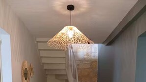Un escalier avec des finitions en bois, un luminaire suspendu en fibres tressées et une petite table agrémentée d’une plante.
