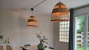 Un coin repas avec une table en bois, des chaises noires, un vase vert et deux lampes en osier suspendues.