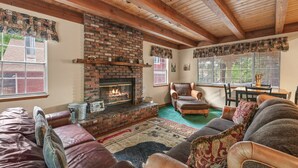 A cozy living room with a brick fireplace, leather sofas, and a dining area with a table and chairs.