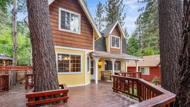 A wooden deck with benches, a covered porch, and large trees.