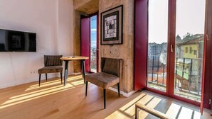 A modern living room with a stone wall, a flat-screen TV mounted on the wall, two chairs, a small round table, and large windows with a city view. - Central Apartments Stay Near Clérigos by HostWise (Porto)