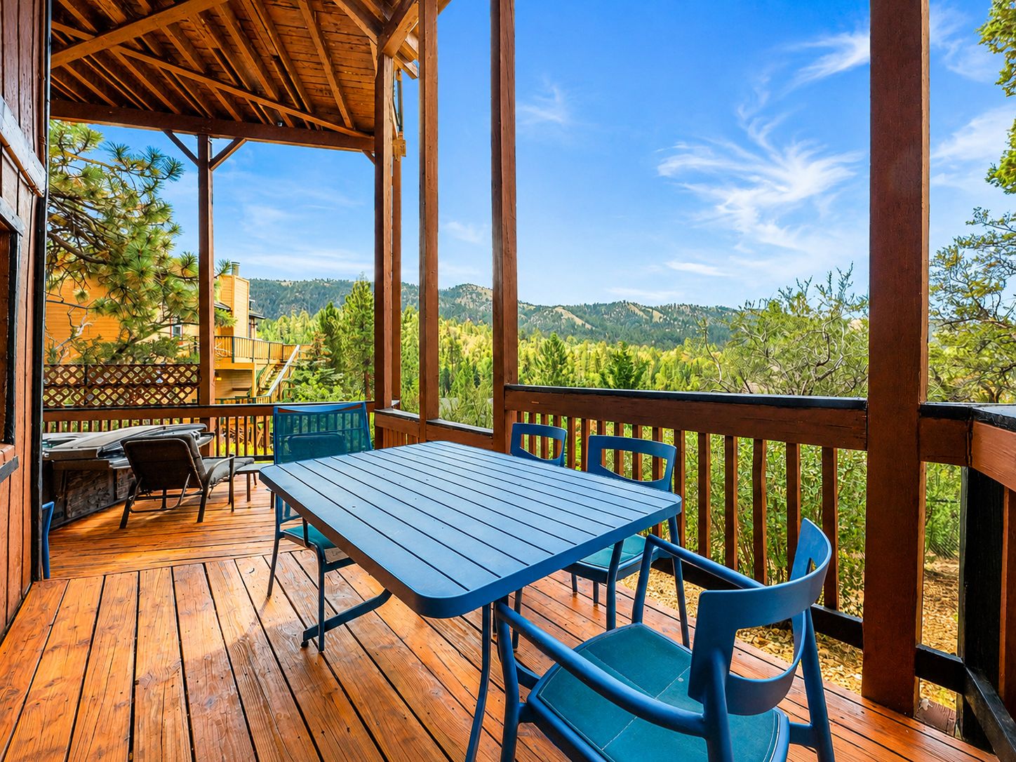 Une terrasse en bois avec une table et des chaises, offrant une vue sur un paysage montagneux.