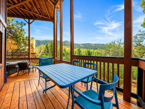 A wooden deck with a table and chairs, overlooking a mountainous landscape.