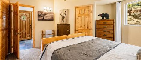 A bedroom with a wooden bed, a dresser, a door, and a window with a view.