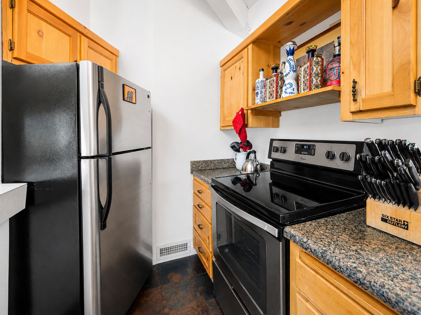 A kitchen with a stainless steel refrigerator, a black stove, wooden cabinets, and a knife block.