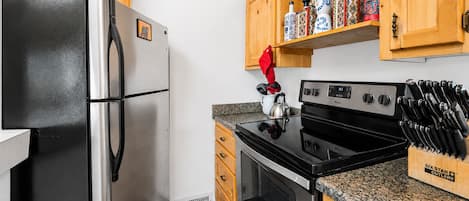 A kitchen with a stainless steel refrigerator, a black stove, wooden cabinets, and a knife block.