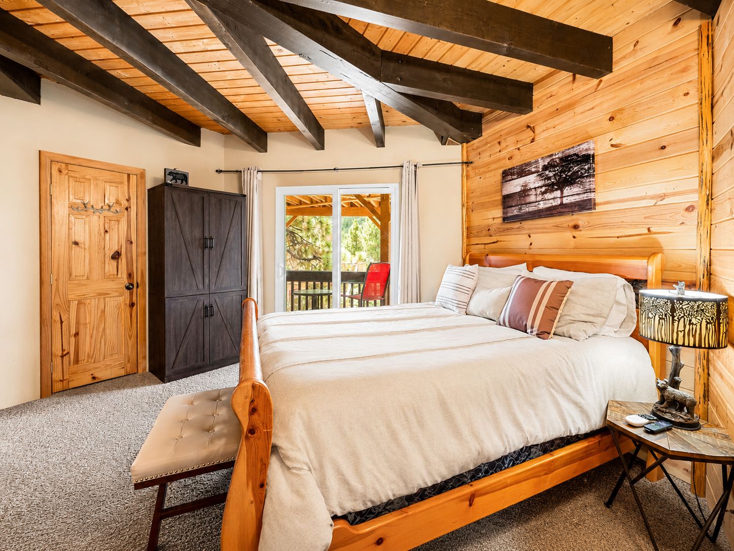 Une chambre à coucher en bois, avec un lit, un banc, une armoire et une table sur laquelle se trouve une lampe.