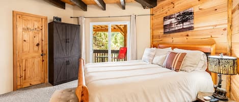 A wooden bedroom with a bed, a bench, a cabinet, and a table with a lamp.