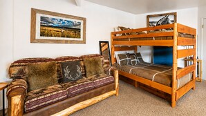 A room with a bunk bed, a sofa with patterned cushions, and a framed landscape painting on the wall.