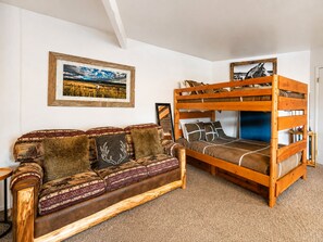 A room with a bunk bed, a sofa with patterned cushions, and a framed landscape painting on the wall.