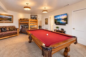 A pool table with a red felt surface, a wooden bench, and a sofa with patterned cushions.