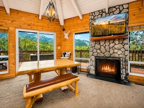 A cozy cabin interior with a stone fireplace, wooden furniture, and a scenic mountain view.
