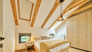 Een slaapkamer met een houten bed, nachtkastje, lamp en raam met uitzicht op groen.