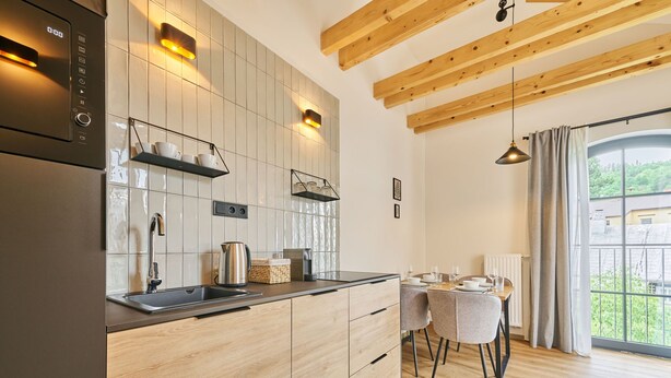 Een moderne keuken met houten kastjes, een inbouwoven en een eethoek met een tafel en stoelen.