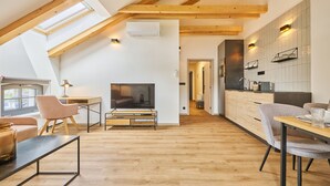 Een modern loft appartement met een schuine plafond, houten balken, een televisie, zithoek en keuken.