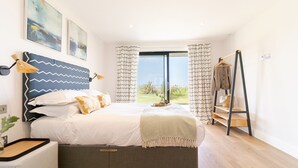 A modern bedroom with a bed, a bedside table, a hanging light, a window with curtains, and a view of the outdoors.