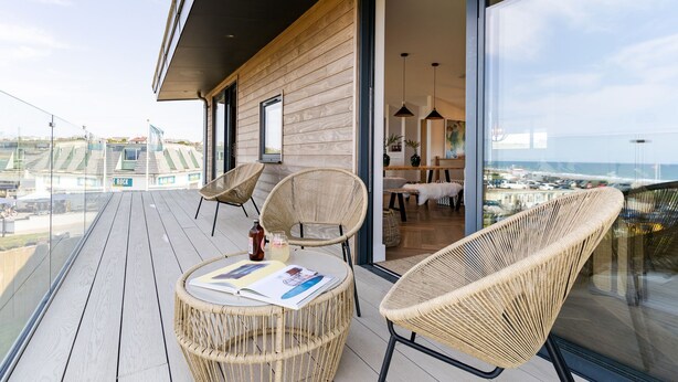A balcony with wicker chairs, a table with a magazine, and a bottle of drink.