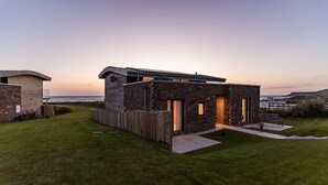 A modern house with a stone facade, a wooden deck, and a view of the sea.