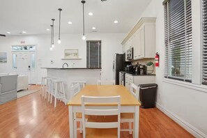 A modern kitchen with white cabinets, a wooden dining table, and pendant lighting.