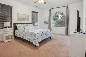 A bedroom with a bed, bedside tables, a TV, and large windows.