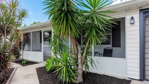 A residential building with a covered porch, a small garden area with various plants, and a visible door. - Cozy Modern Home –Renovated Retreat,Prime Location (Brevard County)