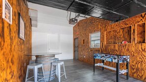 A room with wooden walls, a foosball table, and a bar area with stools. - Cozy Modern Home –Renovated Retreat,Prime Location (Brevard County)