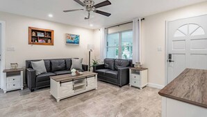 A modern living room with a black leather sofa, a wooden coffee table, and a ceiling fan. - Cozy Modern Home –Renovated Retreat,Prime Location (Brevard County)