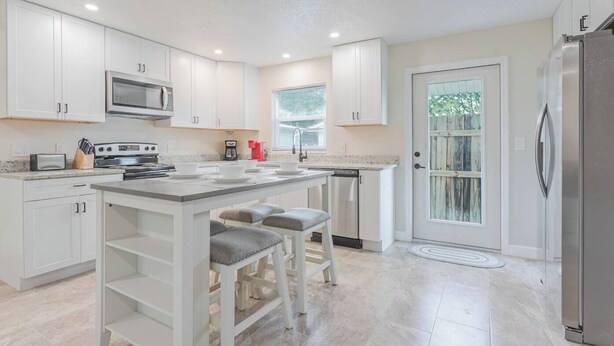 A modern kitchen with white cabinets, a stainless steel refrigerator, a microwave, and a coffee maker. - Cozy Modern Home –Renovated Retreat,Prime Location (Brevard County)