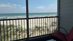 A beach view from a balcony with a railing, beach umbrellas, and chairs. - Ocean Cove 108 - Oceanfront in Garden City Beach (Garden City)