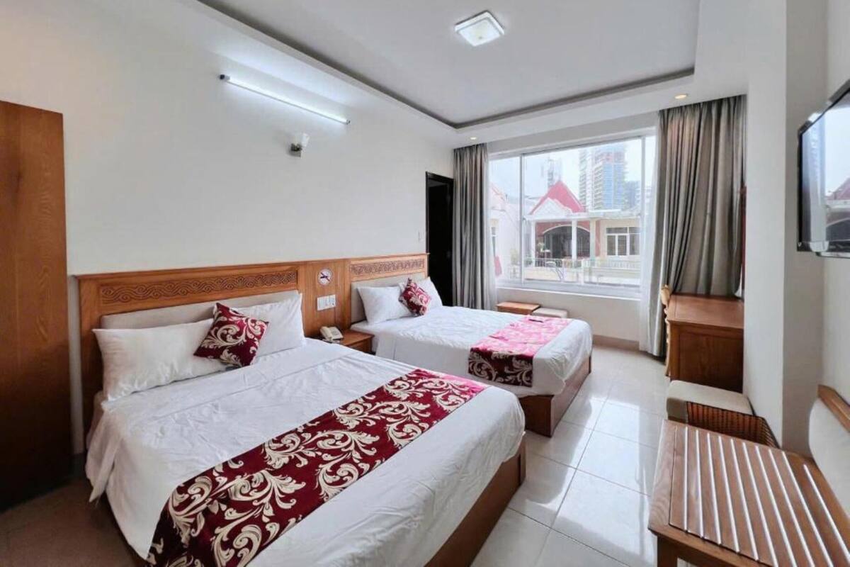 Habitación de hotel con dos camas, cabecero de madera, una mesita y un ventanal con cortinas.