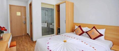 A hotel room with a bed, a wooden headboard, and a glass shower enclosure.